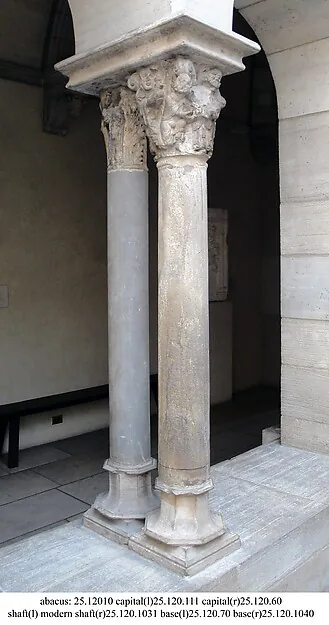 Fotografie zweier steinerner Säulen mit geschnitzten Kapitellen in einem Innenhof; unter dem Bild steht eine Zeile mit Inventarnummern.