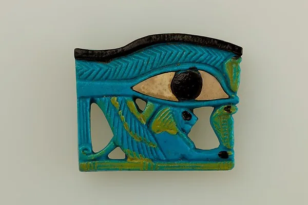 Flaches türkisfarbenes Amulett in Form eines Auges: schwarze Pupille auf hellem Augapfel, darüber eine dunkle Braue, darunter durchbrochene Streifen.